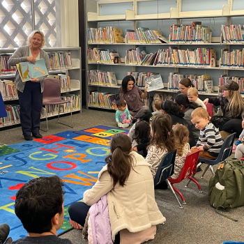 Photo of children listening to a librarian read a story.