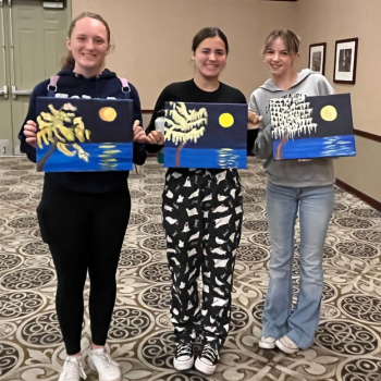 Photo of three teens holding up their paintings.