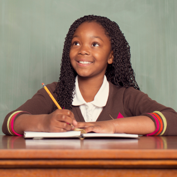 young girl holds a pencil while sitting at a desk with a notebook open in front of her